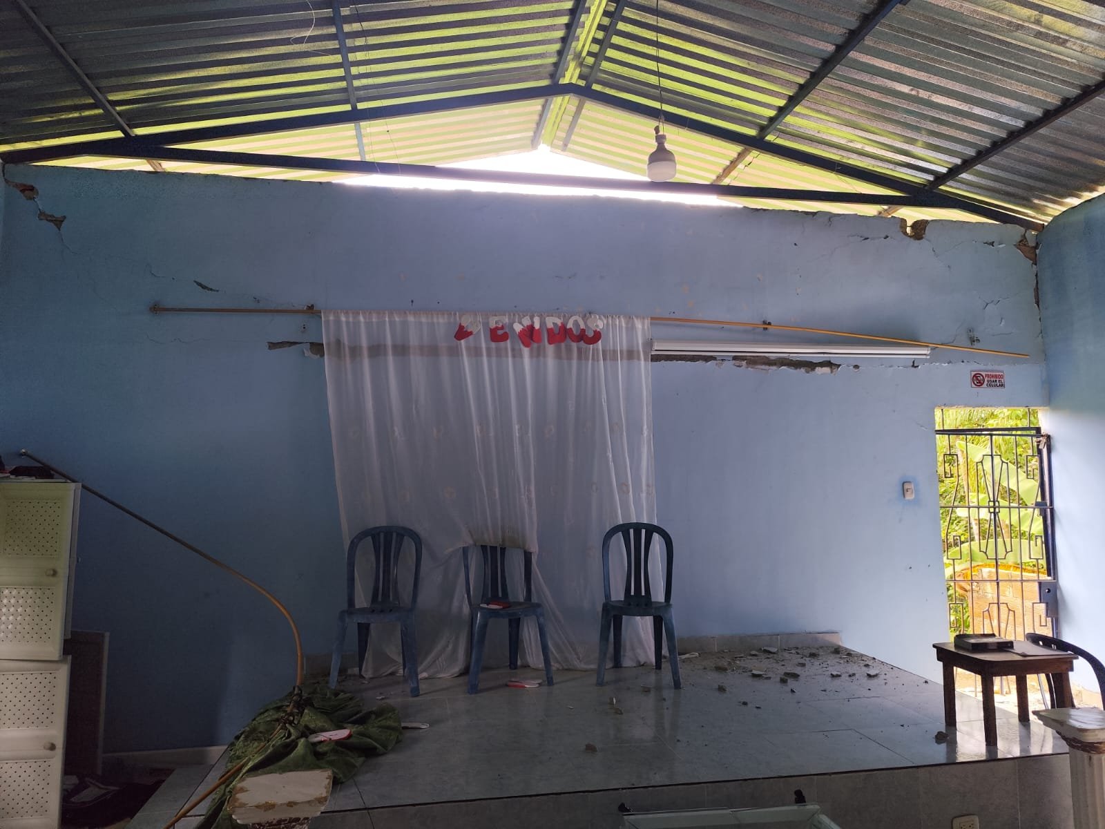 Salón comunitario con pared agrietada junto a puerta metálica